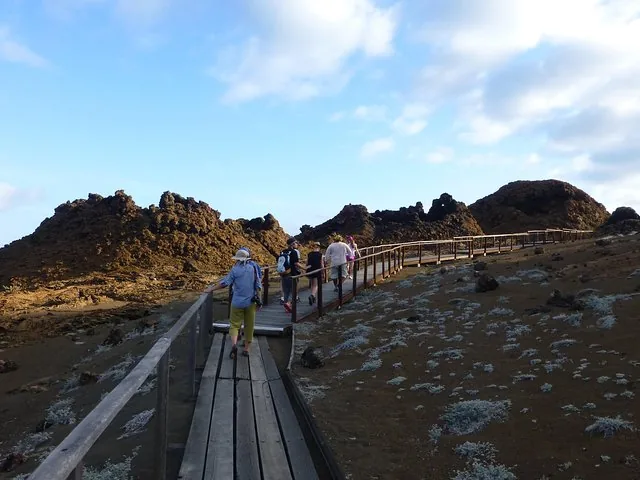 Touristen schlendern auf einem Holzsteg durch die karge Vulkanlandschaft der Bartolomé-Insel.