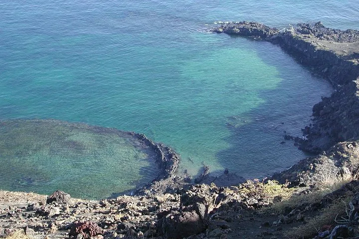 A high-angle view of clear turquoise waters surrounded by dark volcanic rocky shores.