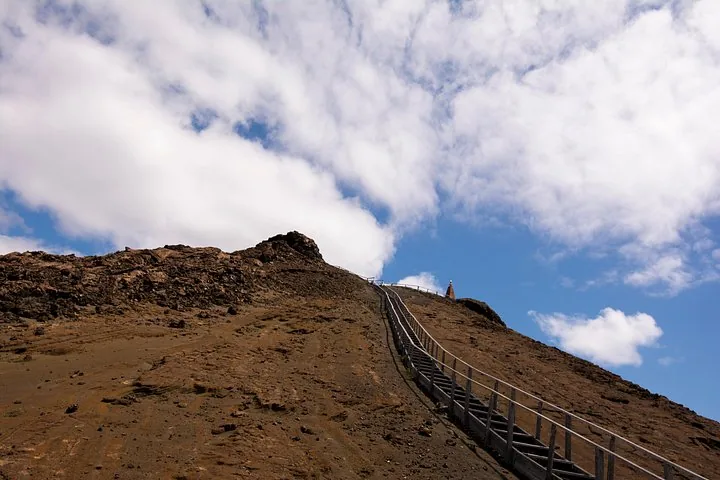 Steep wooden stairs leading up a volcanic hill towards a distant viewpoint.